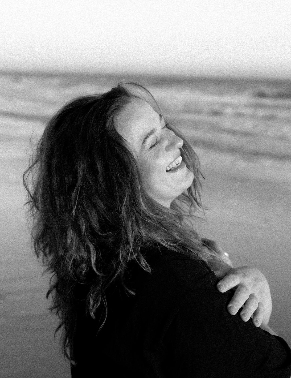 Angie Hagedorn, Hochzeitsfotografin, lehnt sich lächelnd an eine dunkelblaue Hausfassade und hält eine Kamera in der Hand.